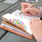 
A girl writing on midori style traveler's notebook with scandi spots and stripes design on a wooden table